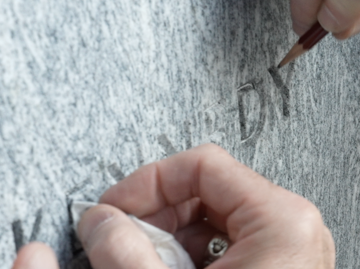 A close-up image of pencil lead being added to the carved letters of the word 